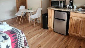 Een knus verblijf met een bed, een eettafel met stoelen, een kitchenette met een magnetron, koffiezetapparaat en vaatwasser.
