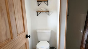 Een kleine badkamer met toilet, een plank erboven en een douchehoek.