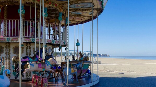 A carousel with horses and a swan, located near a beach with a clear sky.