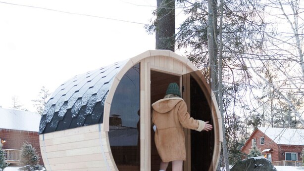 Eine Holzhütte mit Runddesign, eine Person darin und verschneite Umgebung.