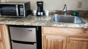 Una cocina compacta con armarios de madera, un refrigerador de acero inoxidable, un microondas, una cafetera y un lavamanos.