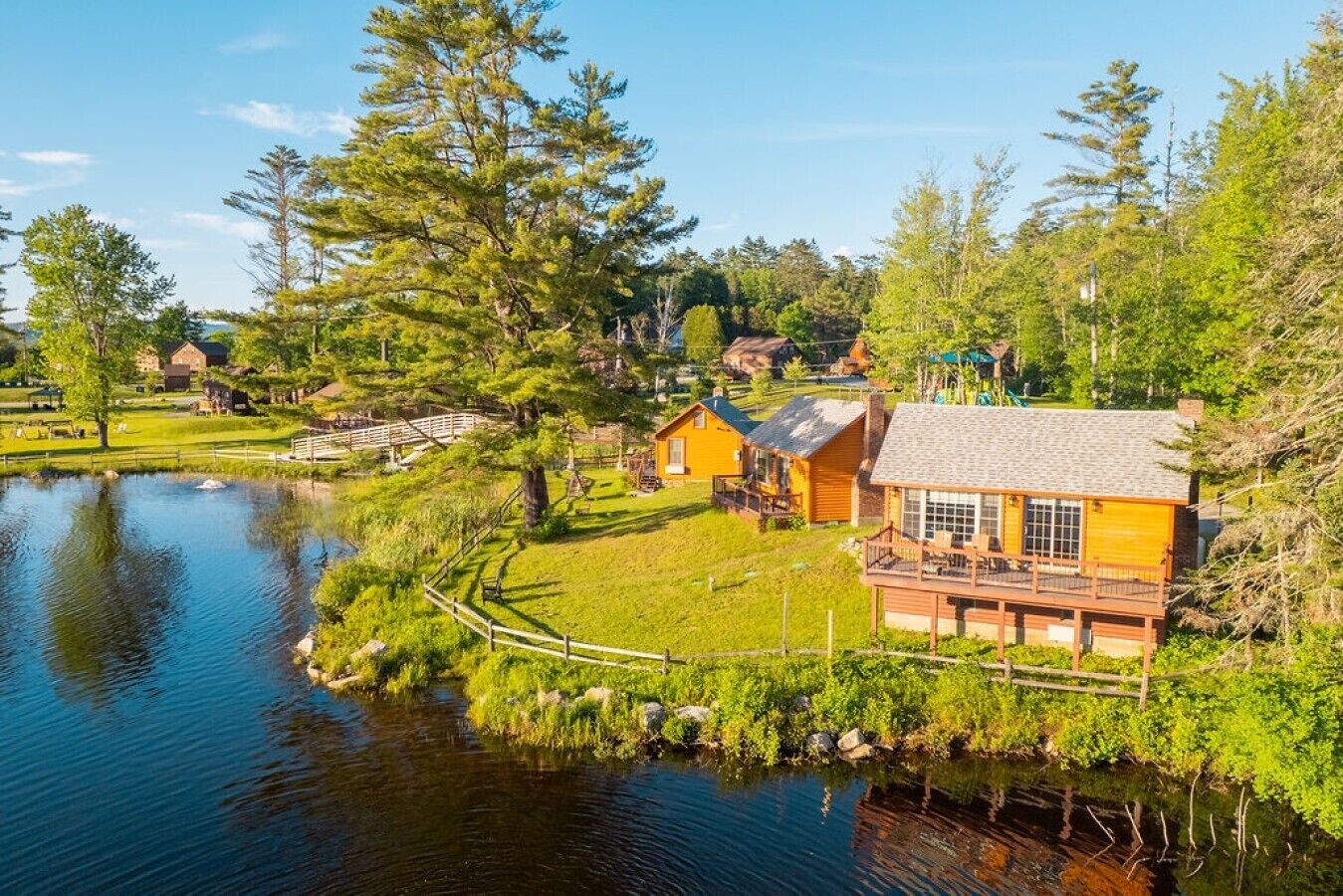 Ein Chalet am Seeufer mit einer Holzterrasse, einem Teich und umgebender Bepflanzung.