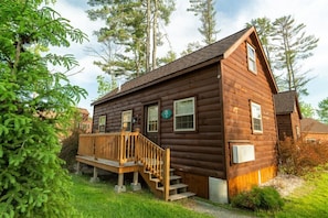 A log cabin with a wooden deck and a single staircase leading to the entrance. - White Mountains Cozy Log Cabin (Bethlehem)