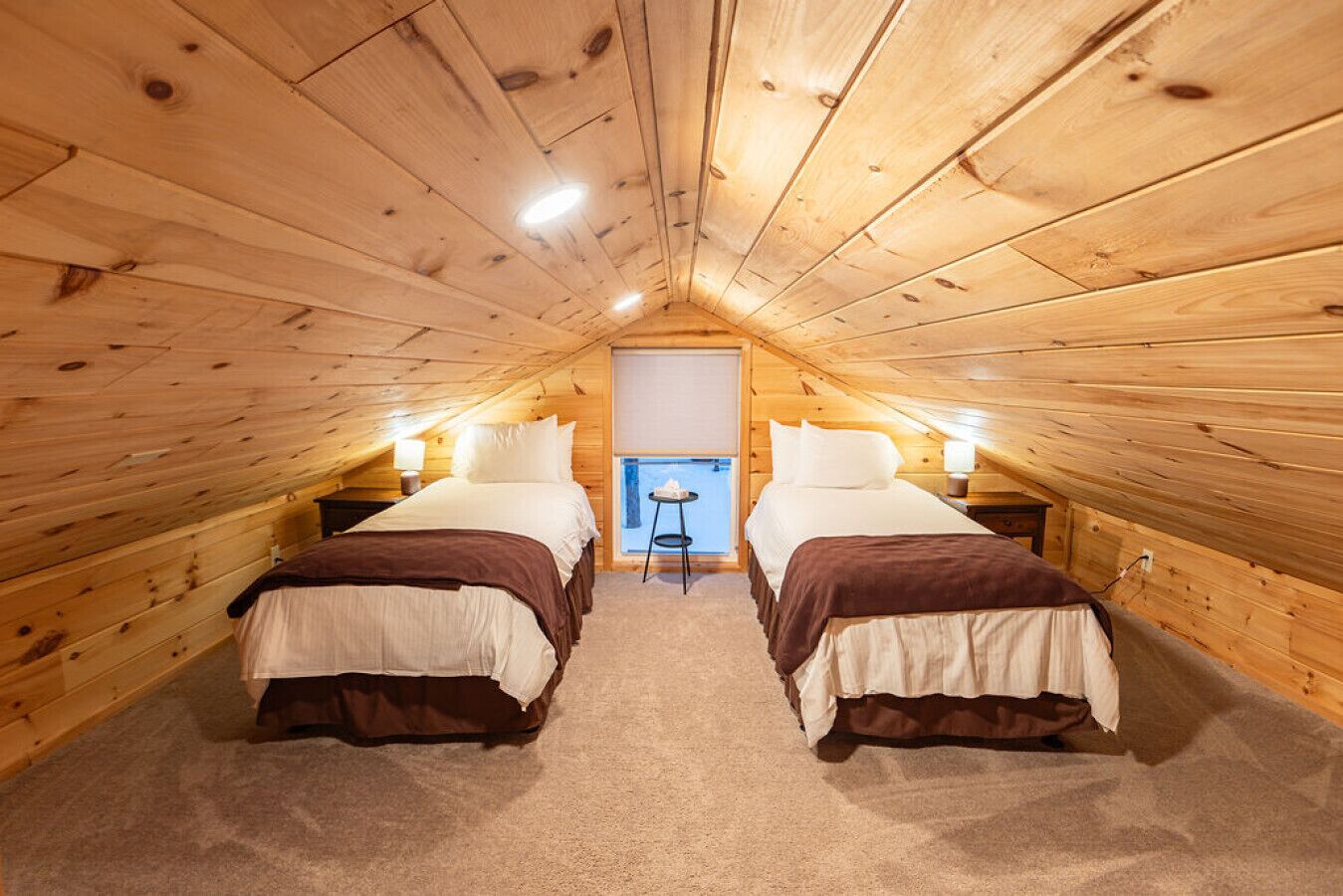 A cozy attic bedroom with two beds, a small table, and a window.