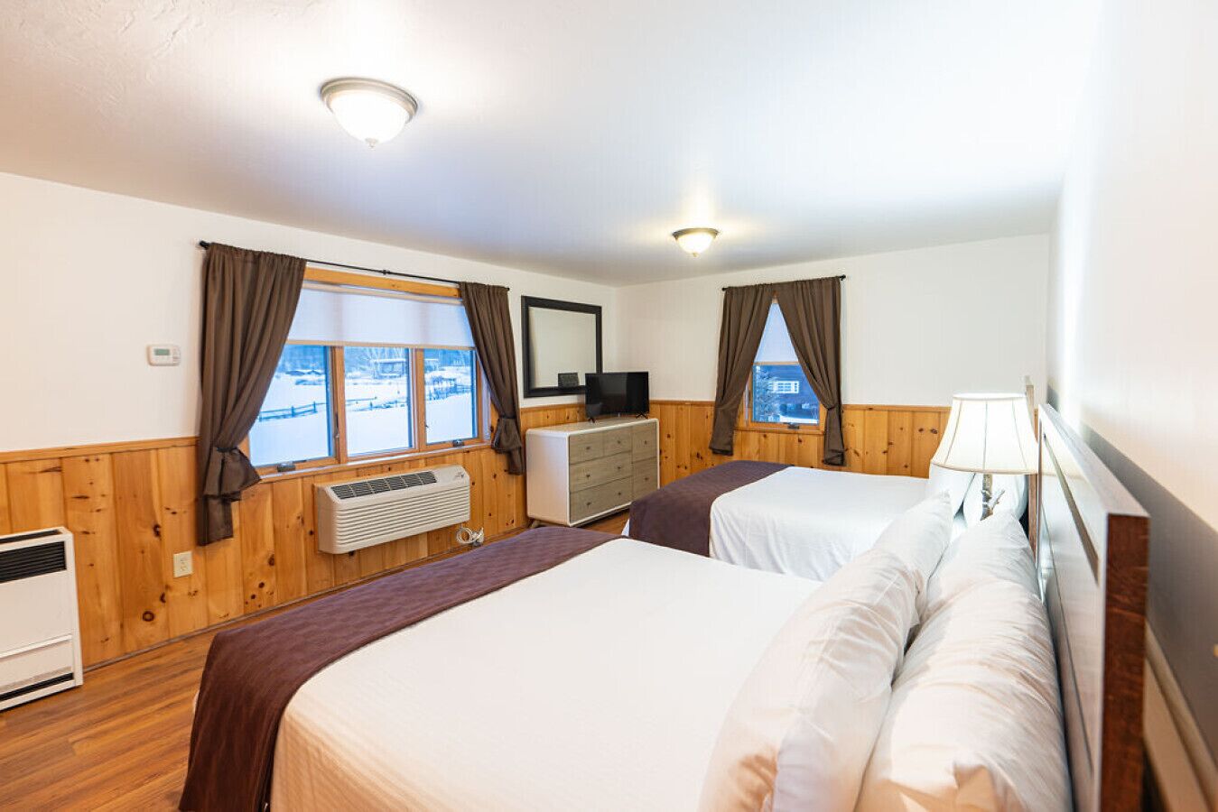 Une chambre d’hôtel avec deux lits, une commode, un téléviseur et un appareil de climatisation.