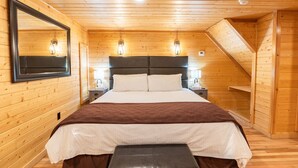 Ein Schlafzimmer mit Holzwandverkleidung, einem Bett, Nachttischlampen, einem Spiegel und einer Bank.