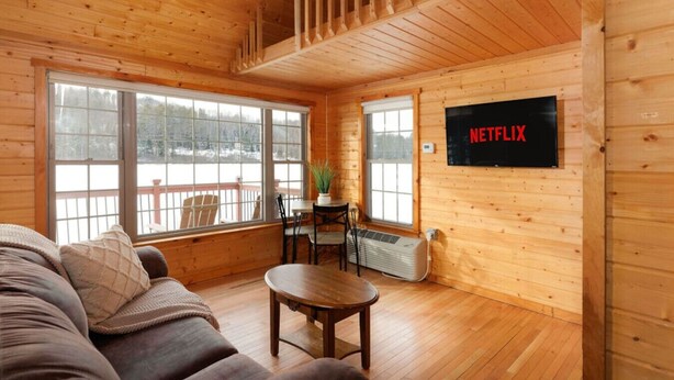 Ein gemütliches Blockhaus-Interieur mit Holzvertäfelung, einer Couch, einem kleinen Tisch und einem an der Wand montierten Fernseher.