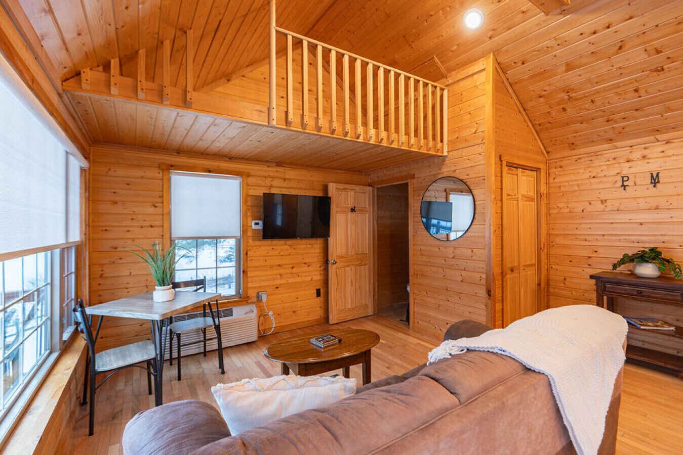 A cozy cabin interior with a dining area, a sofa, a TV, and a mirror.