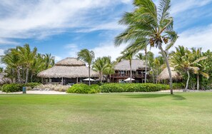 A resort with thatched-roof buildings, palm trees, and a well-maintained lawn.