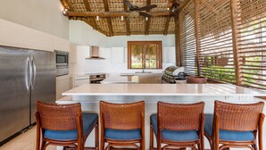 Cozinha com uma ilha grande, eletrodomésticos de aço inoxidável, banquetas de bar de vime e um ventilador de teto.