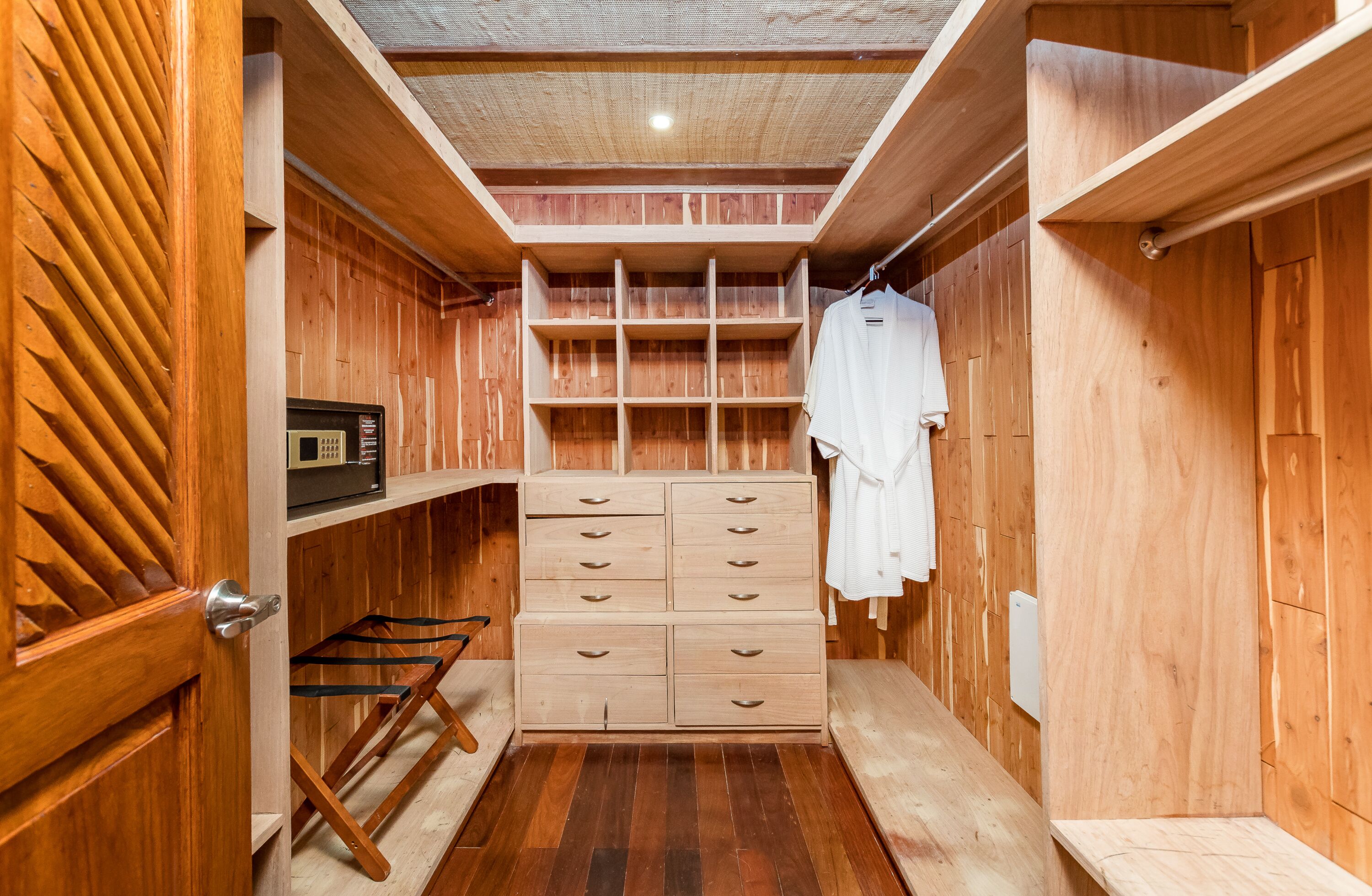 A wooden closet with multiple drawers and shelves, a hanging rack, and a small shelf with a clock.