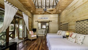 Quarto de cabana de madeira com duas camas, um sofá, uma televisão e um ventilador de teto.