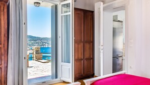 Una habitación con cama, armario y puerta que da a un balcón con vistas al mar y las colinas.