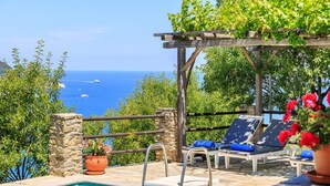 Zona de piscina con una pérgola, sillones de descanso y vistas al mar.