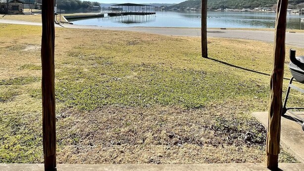 An outdoor area with a concrete floor, a metal railing, and a view of a lake with a bridge in the distance. - Lake front weekend cabin #8 Cabin with kitchen, steps from Possum Kingdom Lake (Graham)