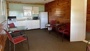 A compact kitchen with a stove, microwave, and refrigerator. There is a ceiling fan, a dining table with chairs, and a wooden wall. - Lake front weekend cabin #8 Cabin with kitchen, steps from Possum Kingdom Lake (Graham)
