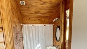 A compact wooden cabin bathroom with a toilet, sink, and shower curtain. - Lake front weekend cabin #8 Cabin with kitchen, steps from Possum Kingdom Lake (Graham)