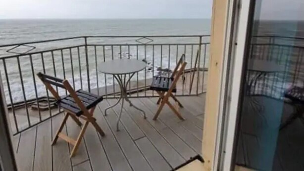 En balkong med ett bord och två stolar, med utsikt över havet.