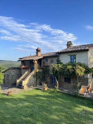 Traditional stone building with a rustic charm, featuring a steep staircase and a small tower on the roof, surrounded by lush greenery and a peaceful outdoor space.