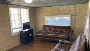 A room with a brown leather couch, a small black table, and a window with blinds.