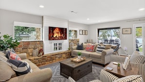 A cozy living room with a stone fireplace, comfortable seating, and a view of the outdoors. - Hottub/Firepit/Lakefront/Outdoor TV/Bunkbeds (Granite Shoals)