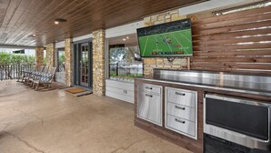 An outdoor patio area with a stone and wood structure, a flat-screen TV mounted on the wall, and a stainless steel grill station. - Hottub/Firepit/Lakefront/Outdoor TV/Bunkbeds (Granite Shoals)