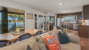 A modern kitchen with stainless steel appliances, a dining area with a wooden table and chairs, and a large window overlooking a body of water. - Hottub/Firepit/Lakefront/Outdoor TV/Bunkbeds (Granite Shoals)