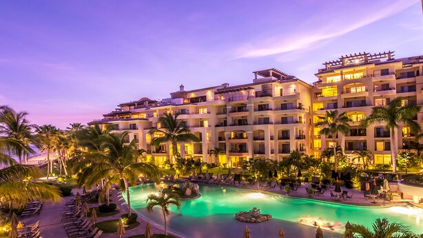 Un hotel con varios balcones, piscina y palmeras.