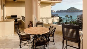 Un balcón con una mesa redonda y sillas, un ventilador de techo y vistas al mar y a las montañas.