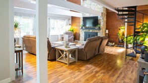 A spacious living room with a stone fireplace, a flat-screen TV, and a wooden staircase. - A-Frame Arbor One Block From The Beach-Four Beds and Four Bathrooms! (Madison)