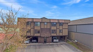 A two-story building with a parking area in front, a sign with the address '17 Jupiter Ave,' and a large brick wall on the right side. - Whitefish Condo, downtown, minutes from Activities (Whitefish)