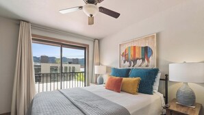 Ein Schlafzimmer mit einem Bett, einem Deckenventilator, einem Fenster mit Vorhängen, einem Bison-Gemälde und einer Lampe auf einem Nachttisch.
