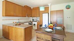 A kitchen with wooden cabinets, a built-in oven, a washing machine, and a dining area with a table set for two. - Modern Apartment with Pool – Albufeira (Albufeira)