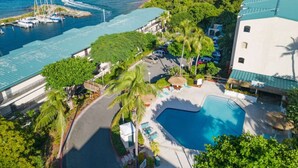 En vy från ovan av ett semesterområde med en swimmingpool, parkerade bilar och en småbåtshamn med båtar.