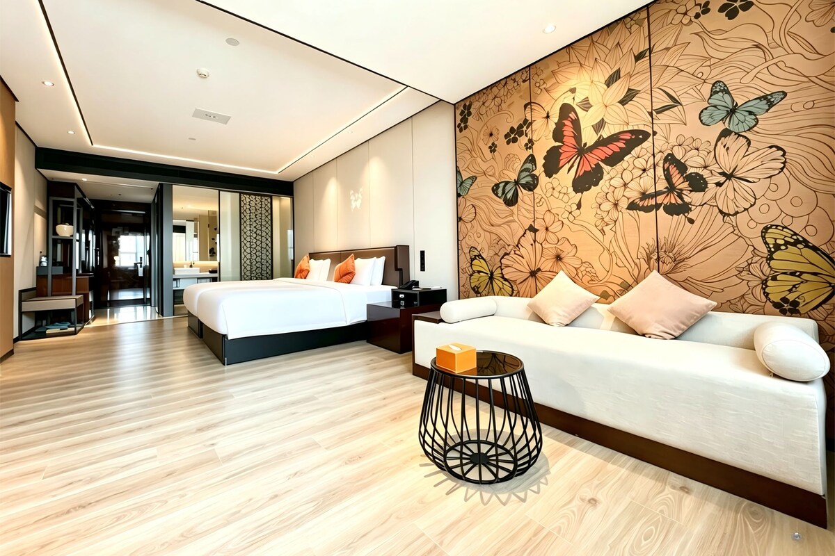 A modern hotel room with a bed, a sofa, a decorative wall, and a wooden floor.