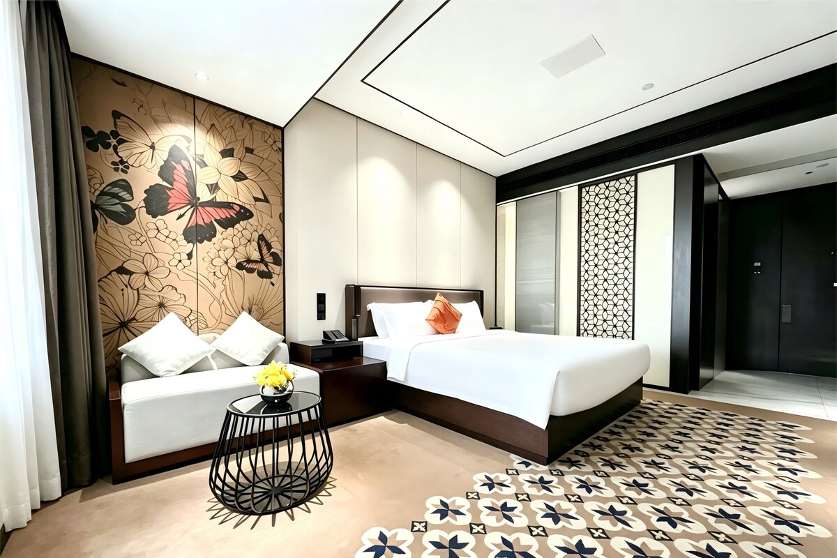 A modern hotel room with a bed, a sofa, a small table, and a decorative wall.