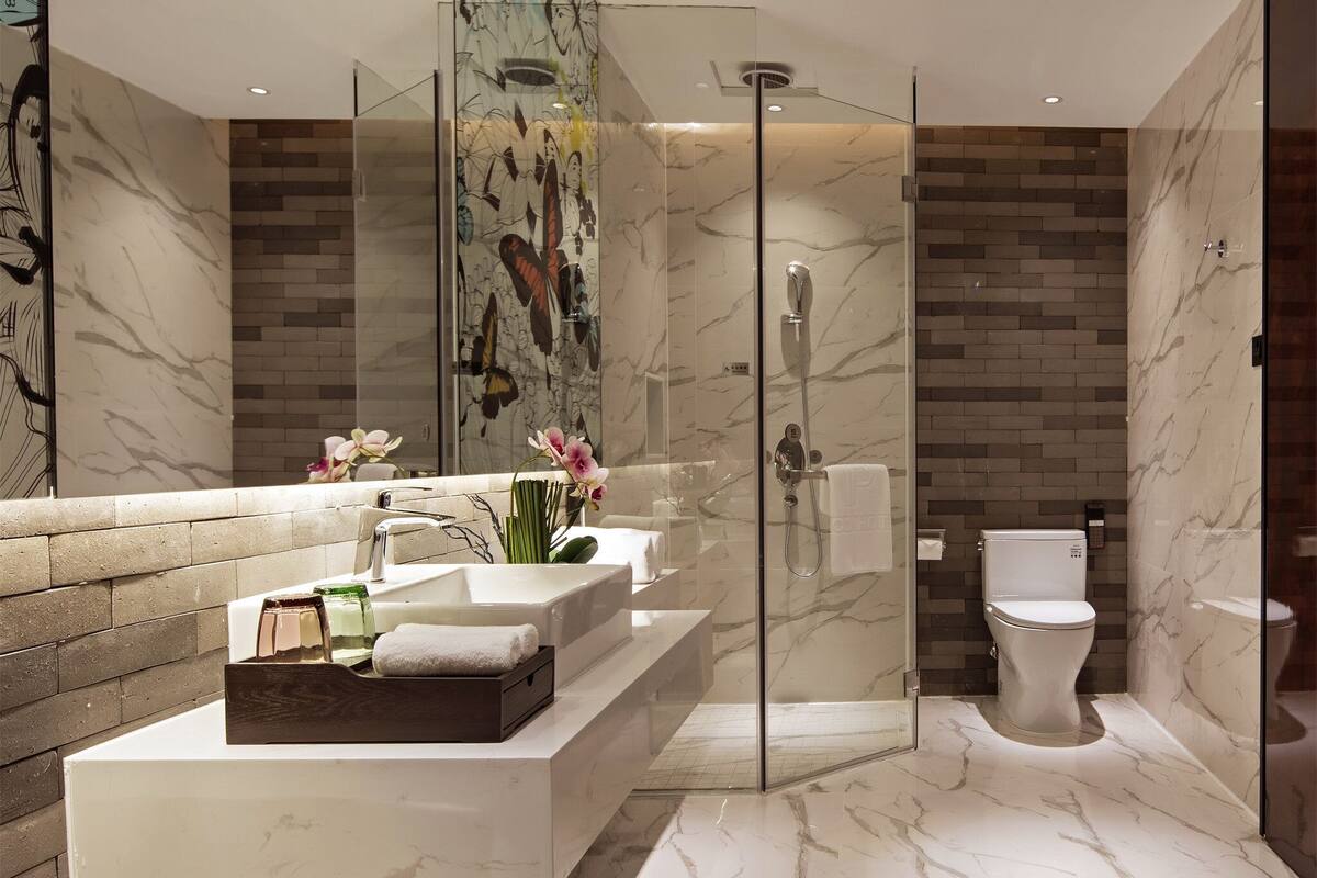 Un baño moderno con ducha de vidrio, piso de mármol y un espejo grande con un mural de mariposas.
