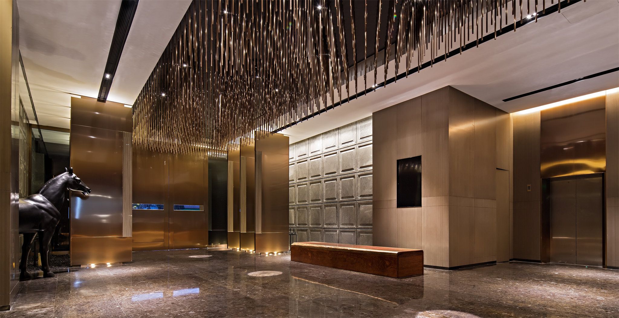 A modern lobby with a metallic horse sculpture, a bench, and a wall with a unique pattern.