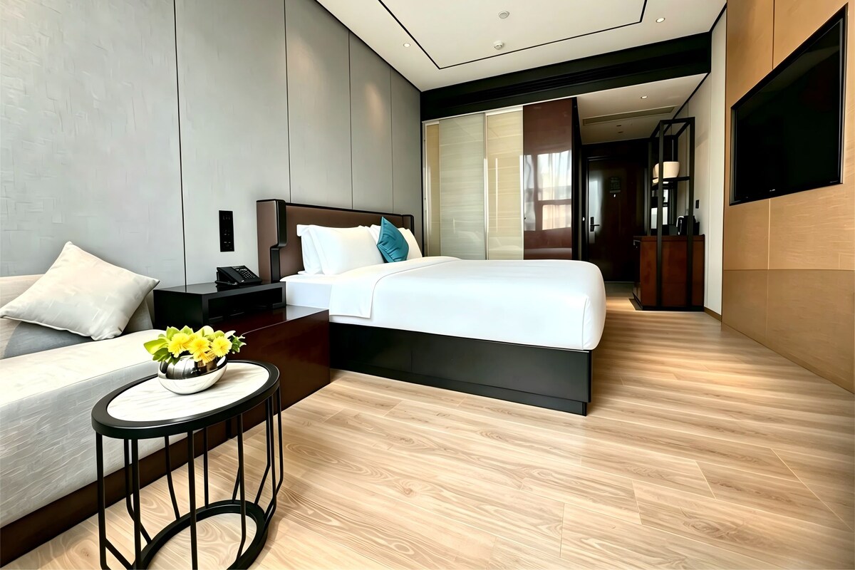 A modern hotel room with a bed, bedside table, and a small round table with a flower vase.