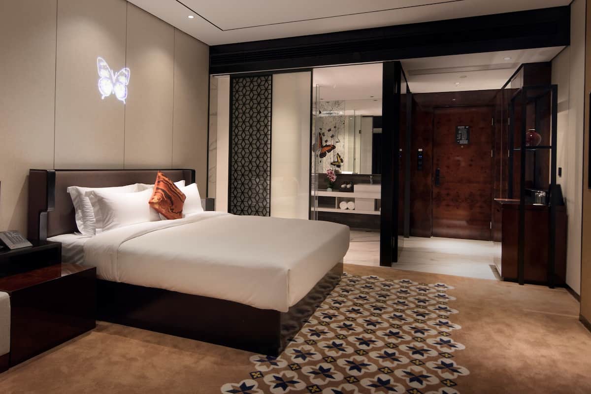 Una habitación de hotel moderna con una cama grande, una mesita de noche, un televisor de pantalla plana y un baño visible a través de una puerta abierta.