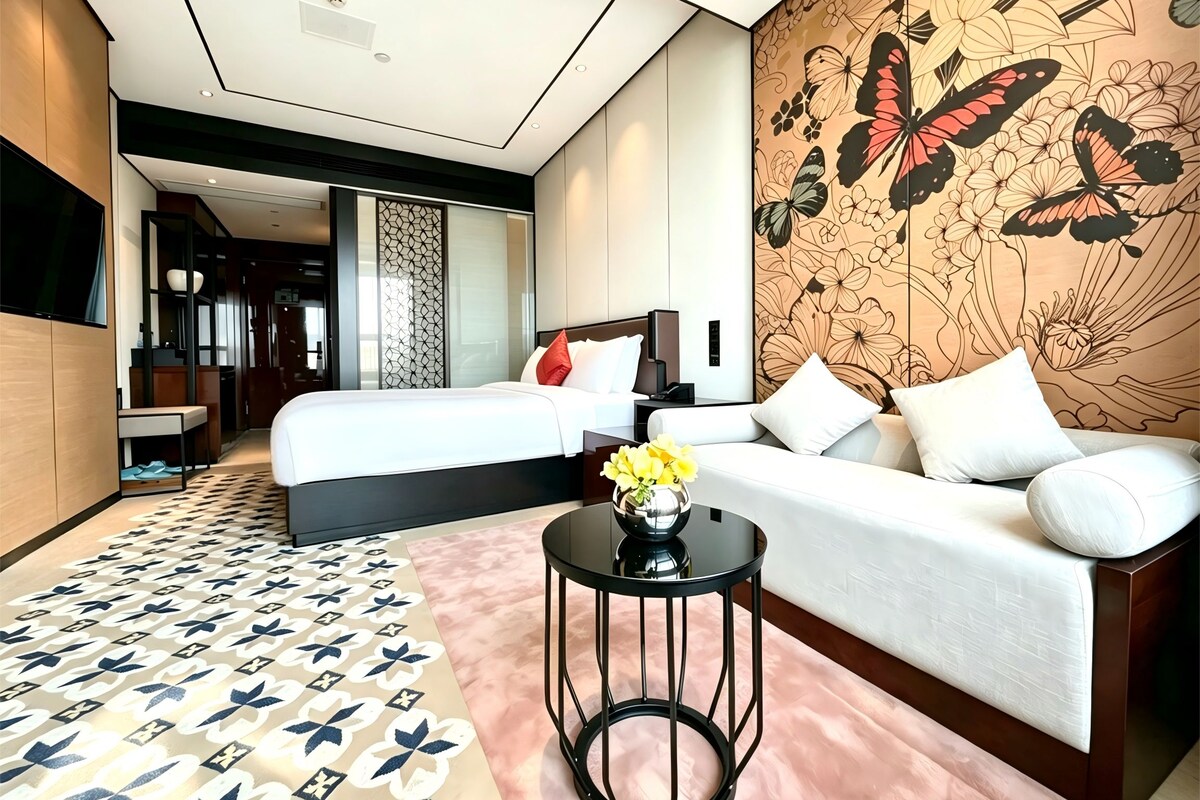 A hotel room with a bed, a sofa, a small table with a vase of flowers, and a decorative wall with a butterfly design.