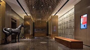 A modern hotel lobby with a horse sculpture, a bench, and a digital display on the wall.