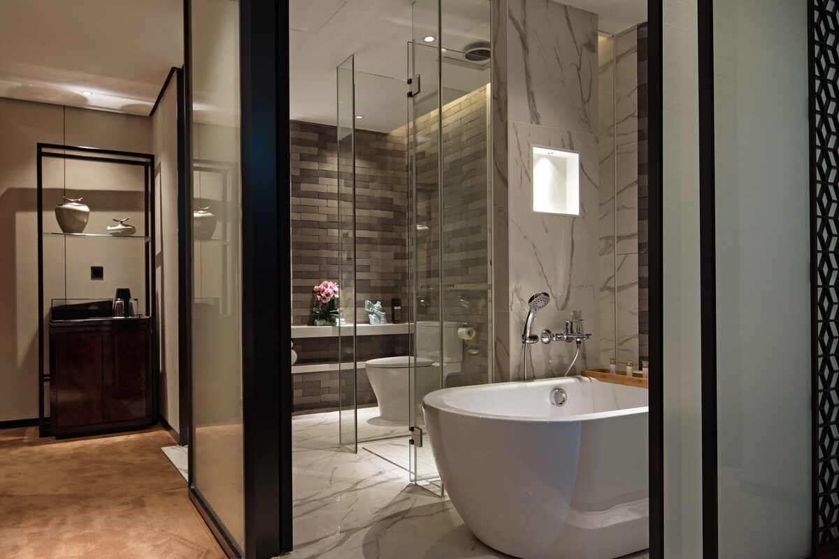 A modern bathroom with a freestanding bathtub, glass shower enclosure, and marble flooring.