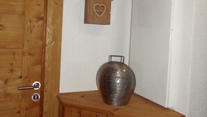 Eine Holztür mit Metallbeschlag, ein Holzkasten mit zwei Schubladen, eine Ziervase, ein kleines Holzhaus mit Herz-Aussparung und ein Regal mit einer Figur.