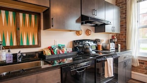 A modern kitchen with dark wood cabinets, a stainless steel range, and a brick wall. - Thompson 212 · Thompson Block Loft - Modern and Historic (Ypsilanti)