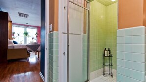Casa de banho com chuveiro, um pequeno armário com produtos de higiene e vista para uma área de estar com sofá e plantas.
