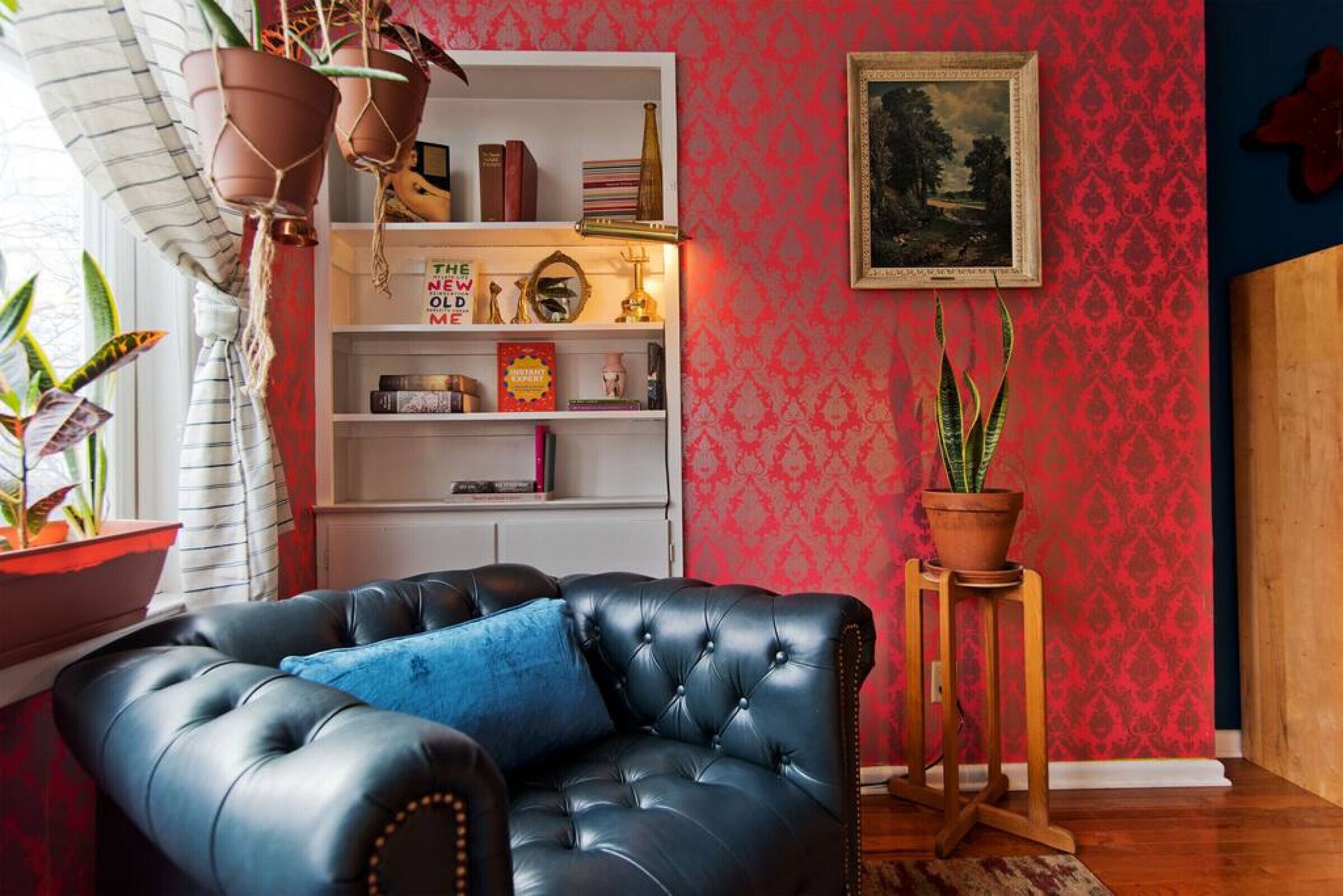 Un salon avec un canapé en cuir noir, une bibliothèque, une plante en pot et un tableau encadré accroché au mur.