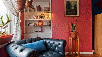 Un salon avec un canapé en cuir noir, une bibliothèque, une plante en pot et un tableau encadré accroché au mur.