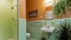 Um banheiro com azulejos verdes, pia branca, vaso sanitário e chuveiro.