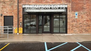 Un edificio de ladrillo con un letrero que dice "THOMPSON LOFTS" y otro letrero amarillo que indica "Lujosos Loft Disponibles Ahora".